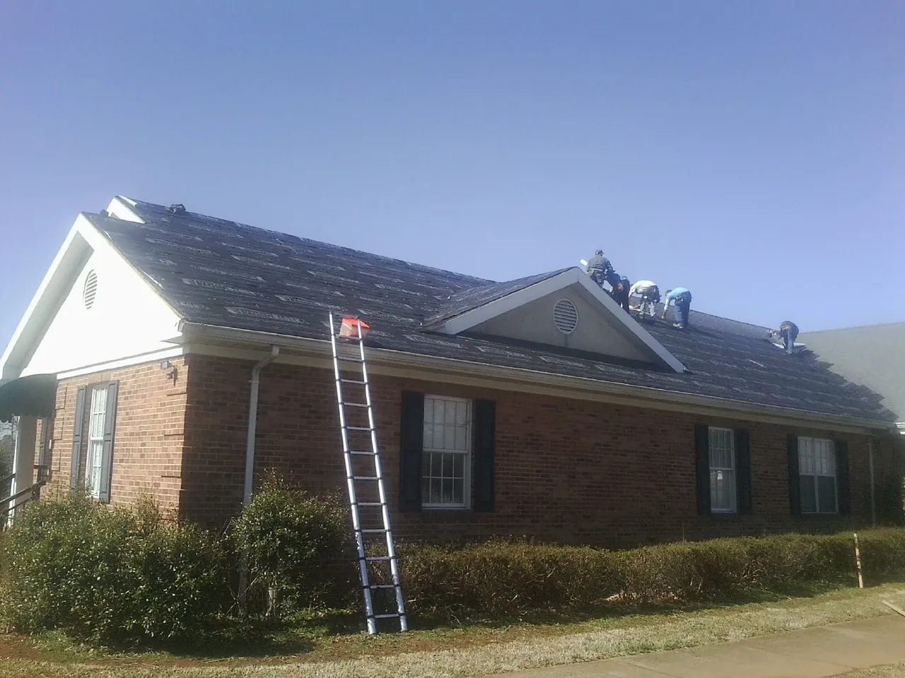 Crew tearing shingles off a brick ranch roof with a ladder set — Emergency Roof Repair work by our crew in Nazareth