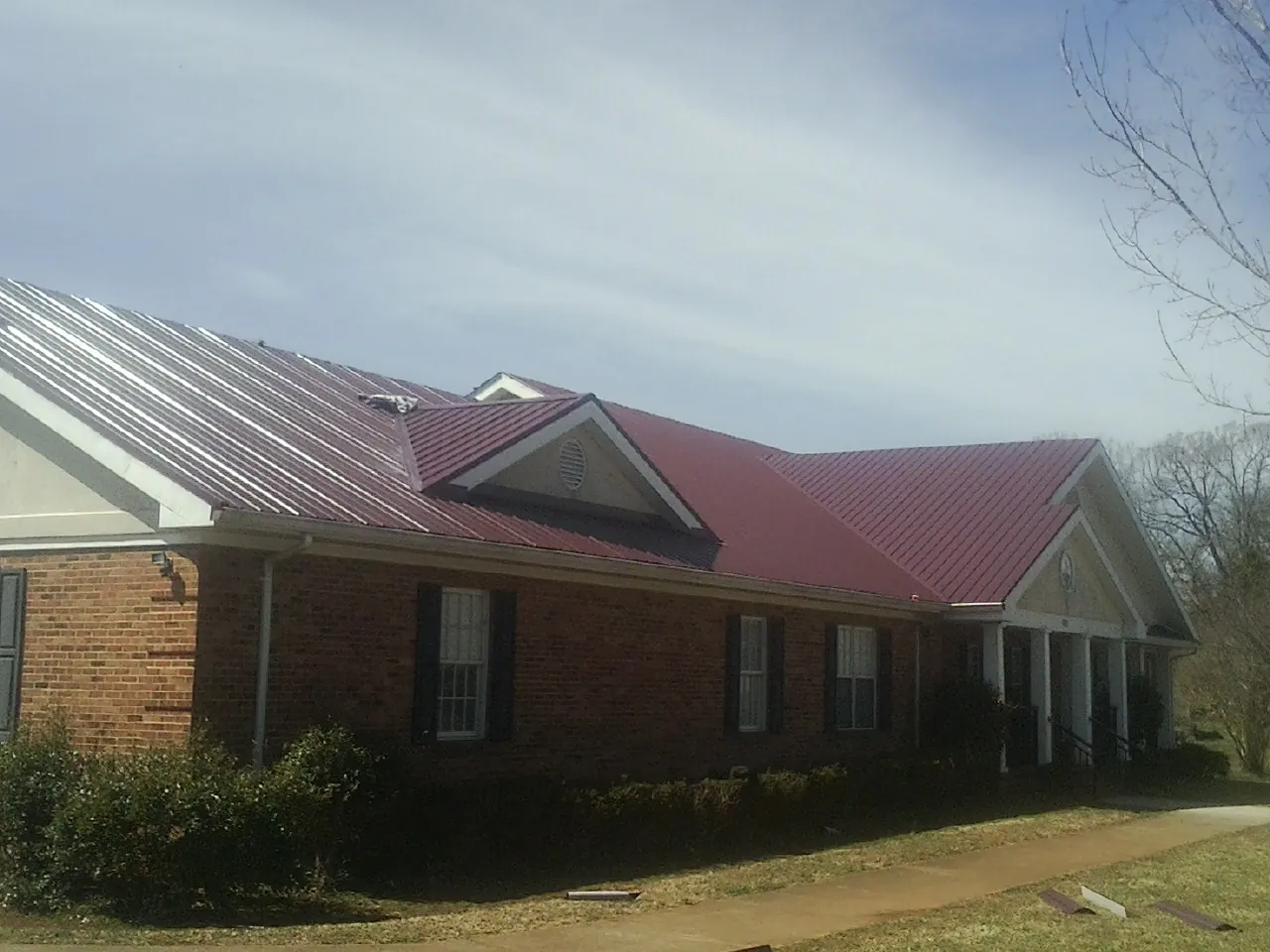 Red metal roof with gabled entries on a long brick building, from a Hail Damage Roof Repair job in Nazareth