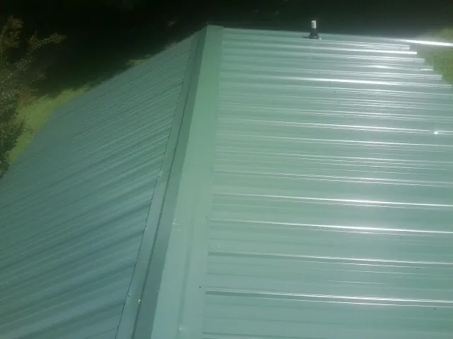 New green metal panels meeting at the ridge of a roof — Flat Roof Repair work by our crew in Nazareth