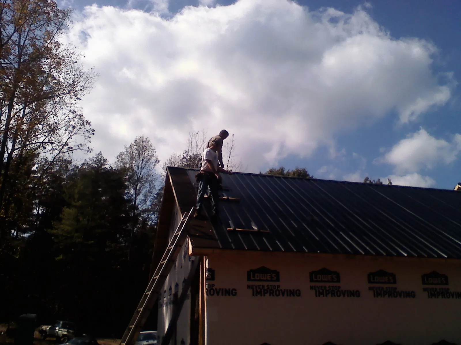Roofer fastening dark metal panels high against a cloudy sky, from a Roof Inspection job in Nazareth