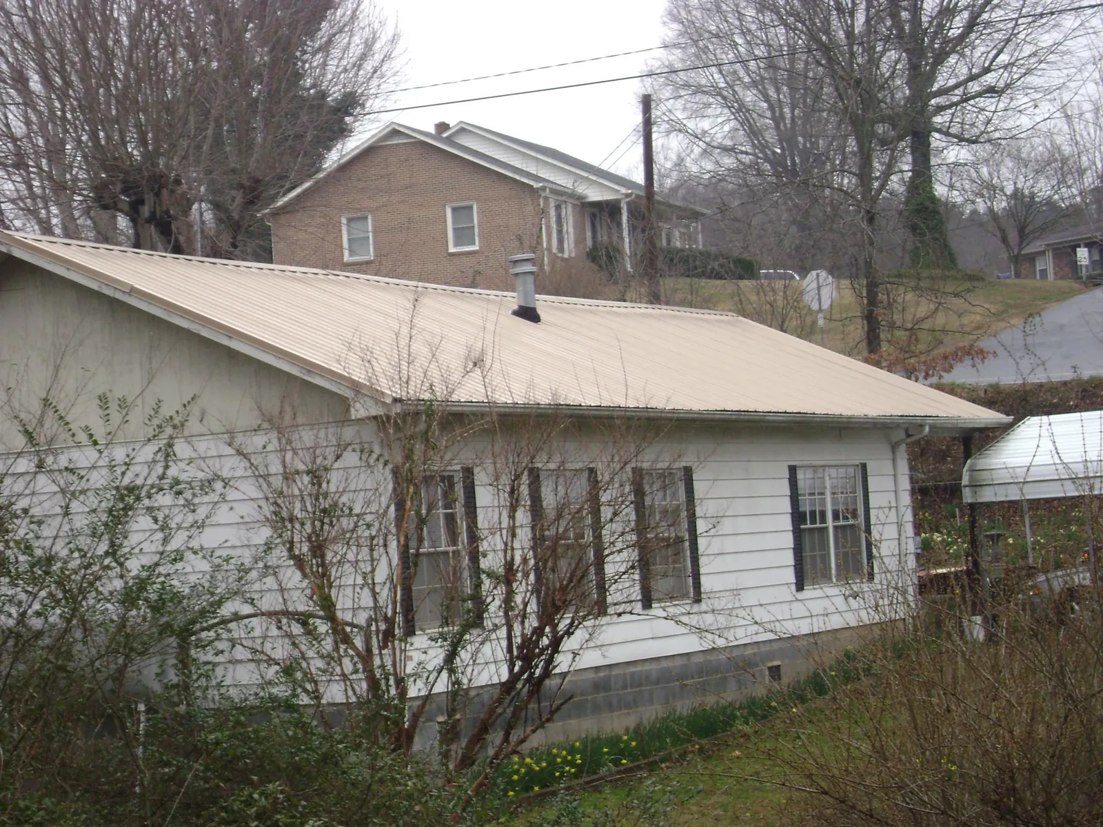 Tan metal roof on a white sided house set into a hillside — Commercial Roofing by Roofing Brothers in Nazareth